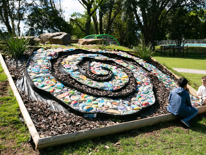 Children beside a painted-stone spiral garden feature in school grounds
