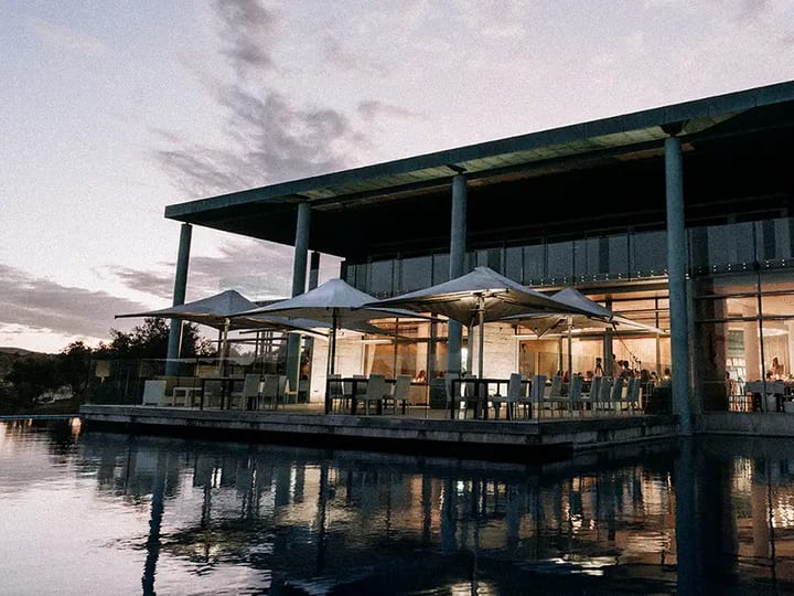 Winery building at dusk reflected in an infinity pool with lit terrace umbrellas