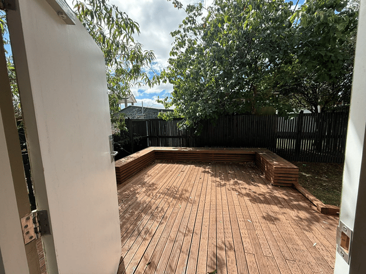 Outdoor timber deck with built-in bench seating and trees beyond fence