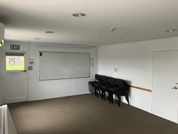 Carpeted room with whiteboard, stacked chairs and exit door