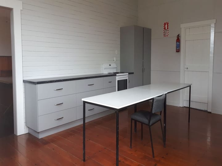 Small kitchen with white drawers, stove, and worktop table, white shiplap walls