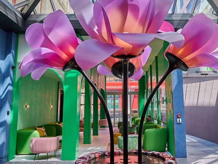 Tall oversized pink flower sculpture with green columns and lounge seating beyond, glass atrium