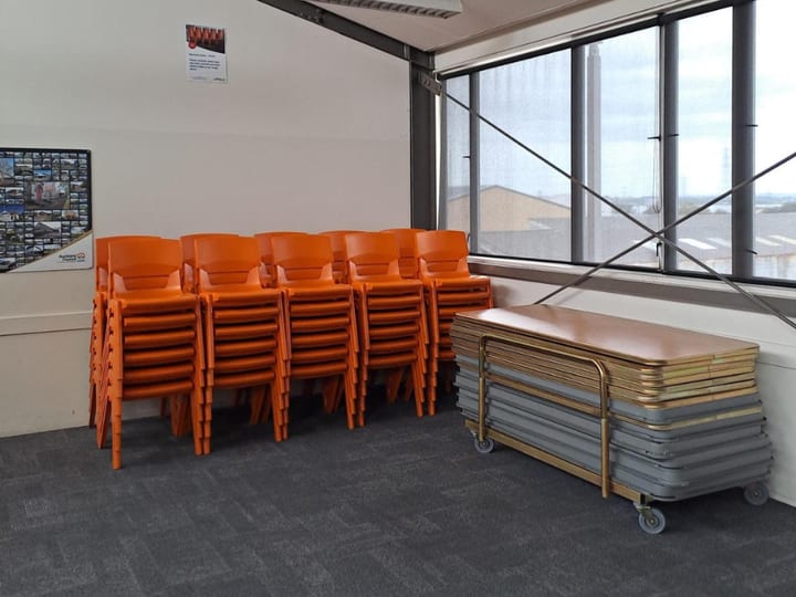 Empty room with stacked orange chairs and folded tables against the wall