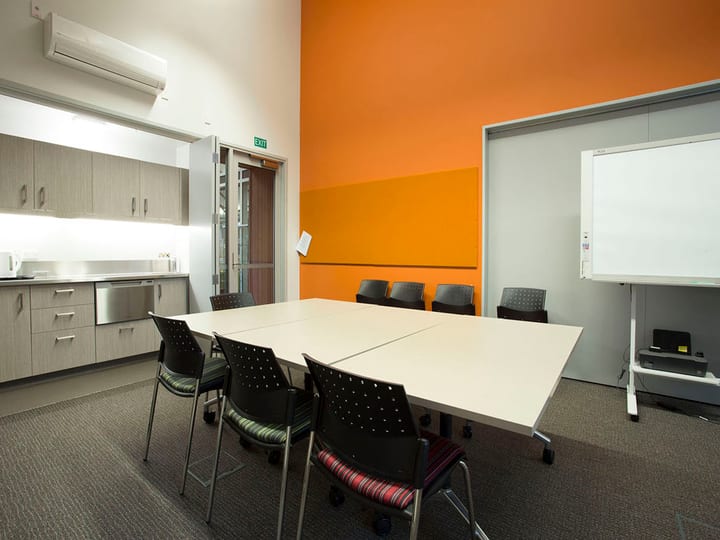 Small meeting room with orange wall, table, chairs and whiteboard