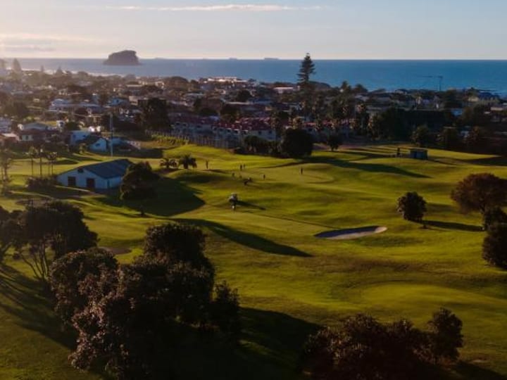 Aerial view of golf course fairways with coastal town and sea beyond