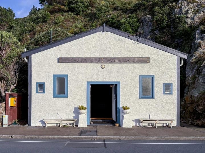 White rendered hall with blue trim and timber sign above entrance