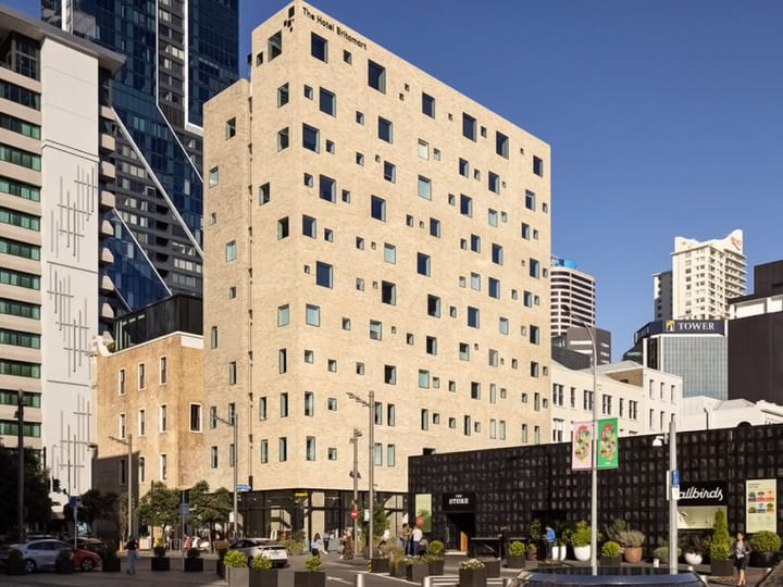 Pale brick building with irregular windows facing city square, daytime street-level view