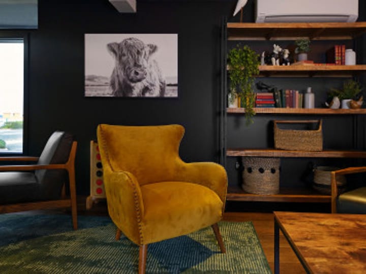Dark lounge corner with mustard armchair, shelving unit and framed artwork