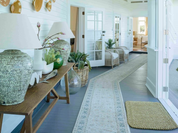 White-painted corridor with runner rug, wicker lamps and woven baskets on wall, doors to rooms
