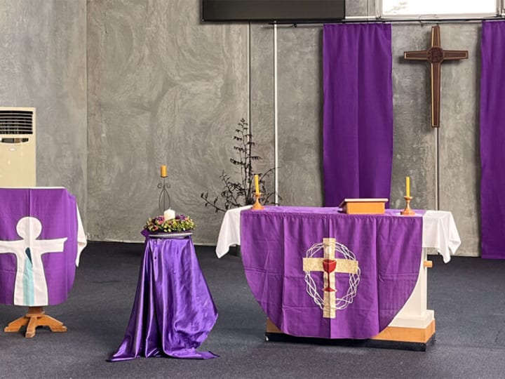 Church sanctuary interior with altar table draped in purple, wooden cross, and candles