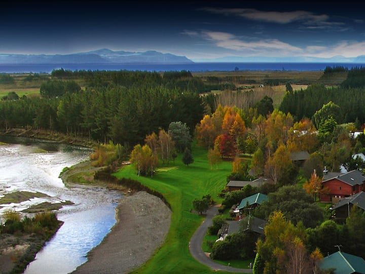Aerial view of lodge buildings among autumn trees beside a river, lake in background