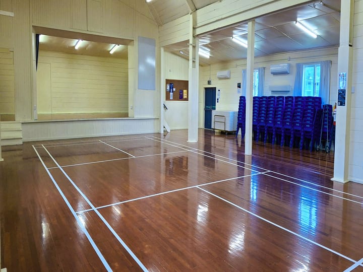 Main hall with polished timber floor, raised platform and stacked chairs