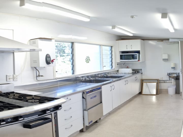 Catering kitchen with white cabinetry, stainless steel benches, gas cooktop and microwave