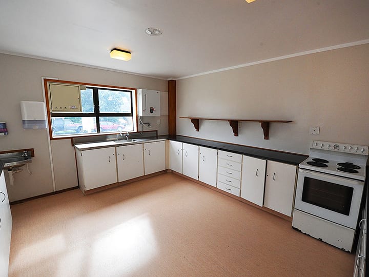 Plain kitchen with white cabinetry, dark benchtop, stove, and wall shelving