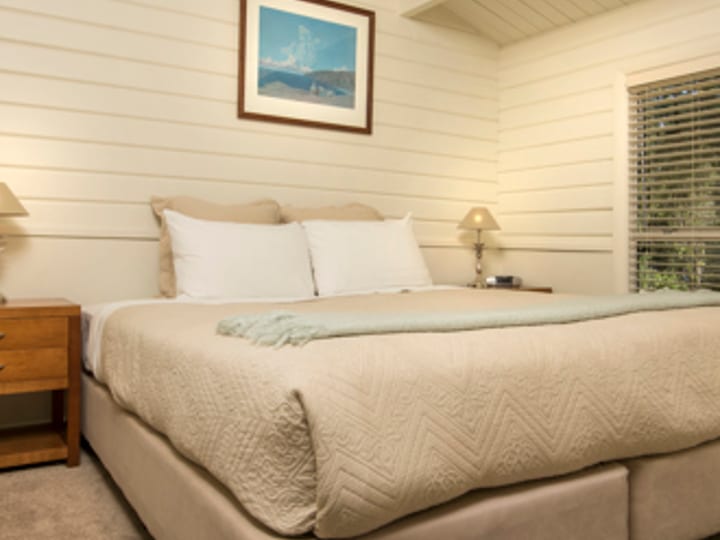 King bedroom with beamed ceiling in timber-lined cottage