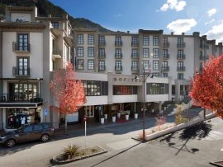 Pale multi-storey hotel building on a street corner with trees and mountains behind
