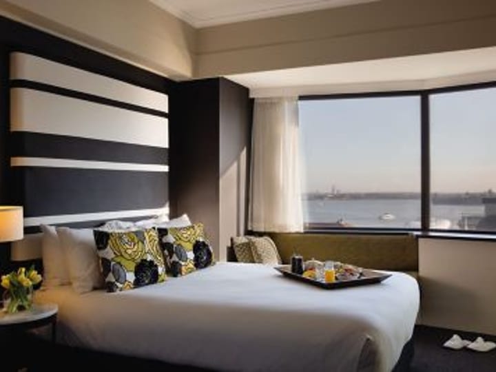 Hotel room with monochrome striped headboard, patterned cushions, and large harbour-view window