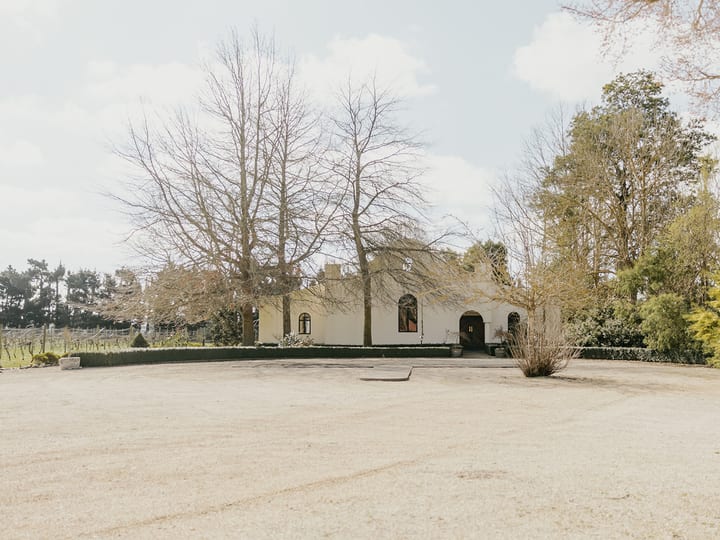 White rendered venue building with arched windows surrounded by bare deciduous trees and vines