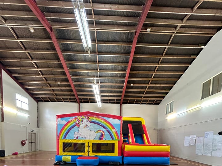 Open sports hall with metal roof structure, bouncy castle, and scattered balloons