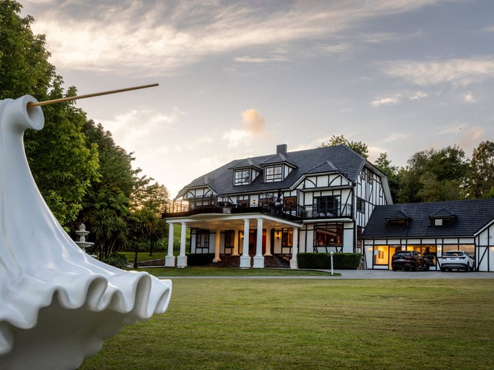 Tudor-style manor house and grounds at dusk with sculpture in foreground