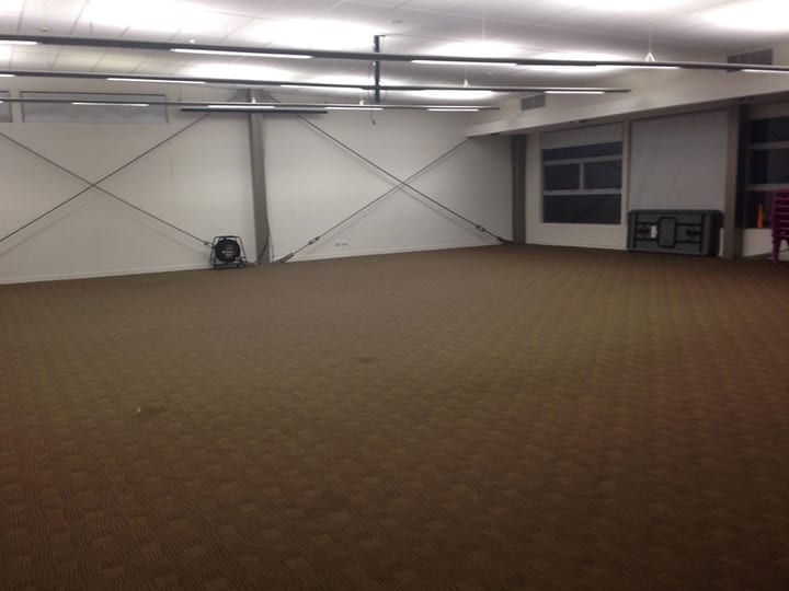 Large empty carpeted hall with exposed bracing cables and high windows