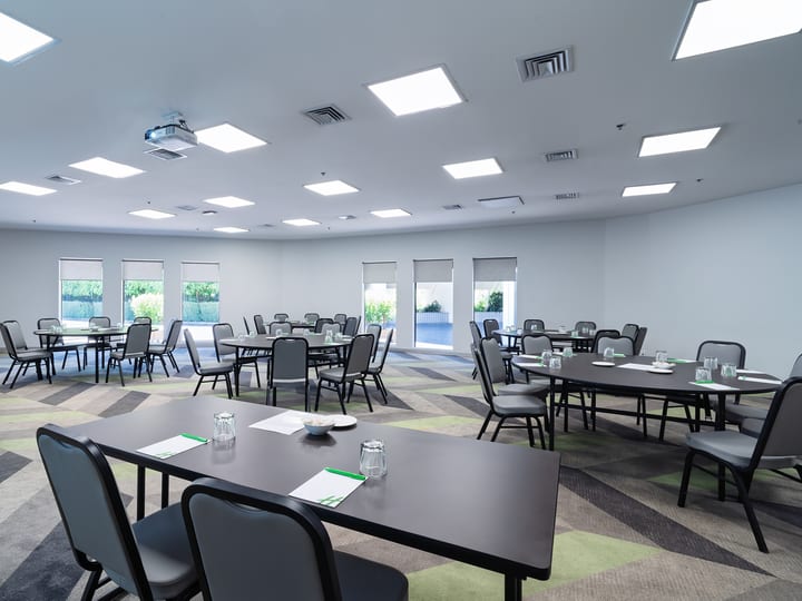 Neutral function room with round and rectangular tables, patterned floor, and row of windows