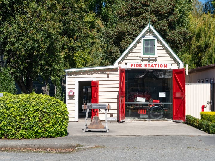 Small heritage Fire Station building with red doors and vintage hand pump