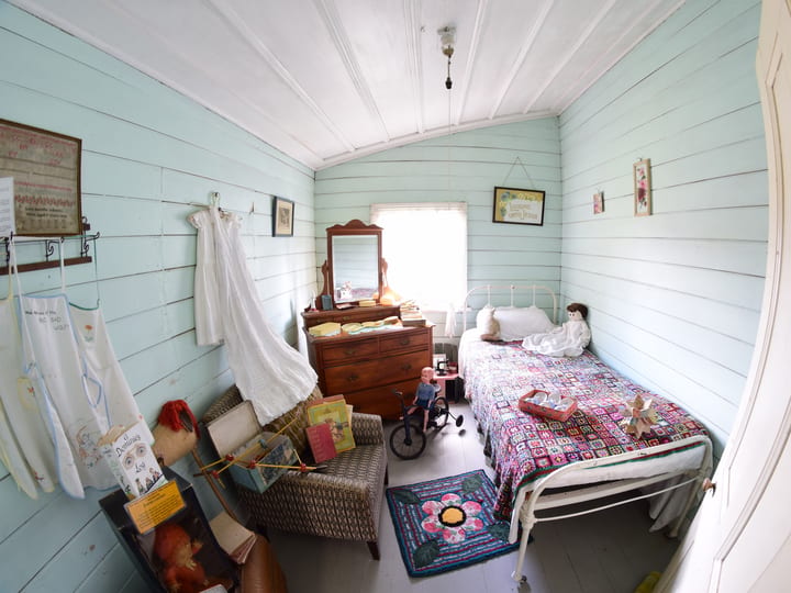 Heritage bedroom with painted timber walls, iron bed, dressmaker's dummy, and period furnishings