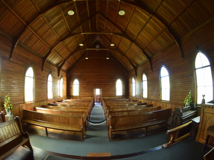 Timber church interior with arched vaulted ceiling, wooden pews, arched windows, and central aisle