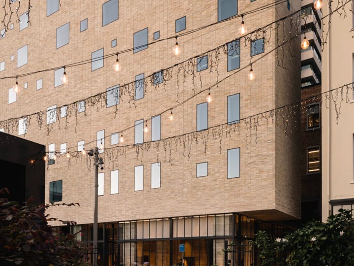 Pale brick building exterior with laneway, string lights overhead and planting at ground level