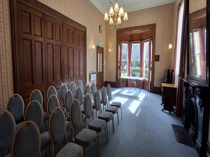 Victorian room with panelled walls, bay window, chandelier and chairs in rows