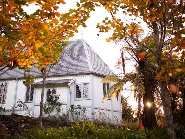 White timber chapel with steeply pitched roof and decorative bargeboards, framed by autumn trees