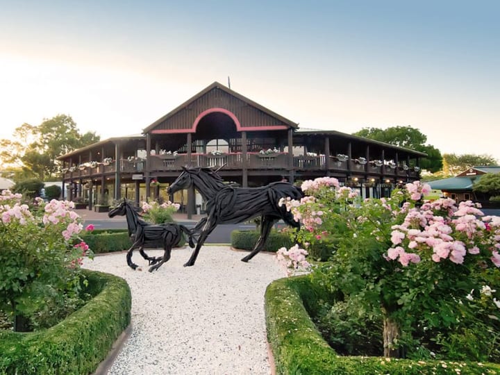 Dark timber two-storey pavilion with a veranda, flanked by formal gardens and horse sculptures