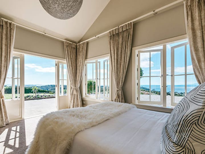 Bedroom with large windows and sea view, neutral tones and draped curtains