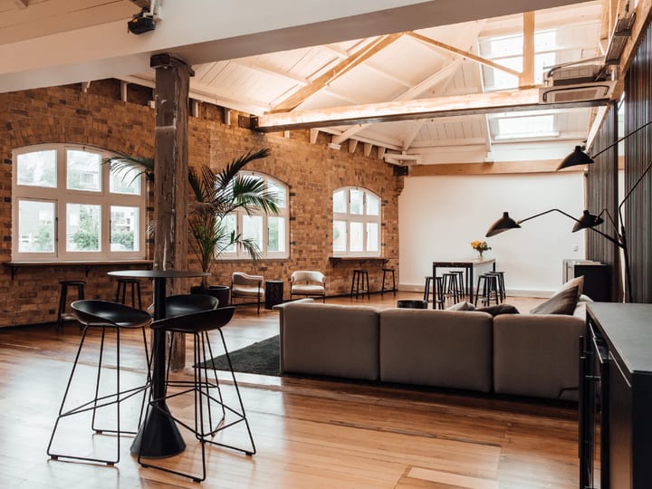 Brick-walled loft interior with exposed timber trusses, timber floor, bar tables and lounge seating