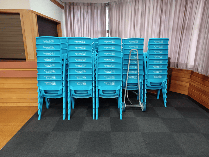 Stacked blue plastic chairs on a carpet floor in a community hall
