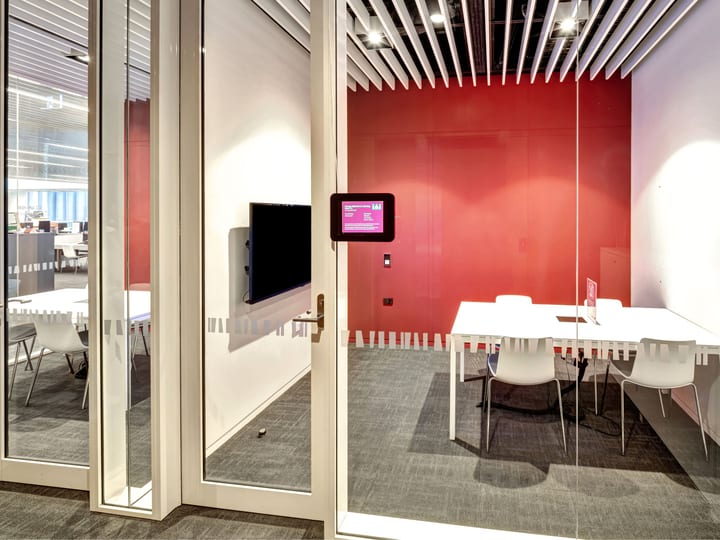 Glass-walled meeting room with red accent wall and white table setting