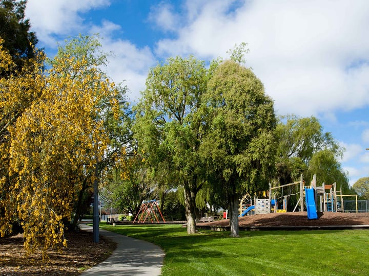 Park with playground equipment and mature trees under blue sky