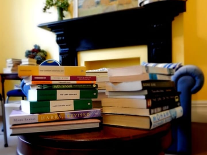 Books stacked on a round side table in front of a fireplace and a leather armchair