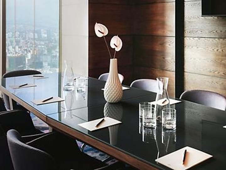Dark-toned boardroom with polished table, upholstered chairs, and floor-to-ceiling city-view window