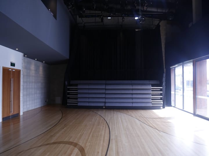 Sports hall with retractable seating folded against curtained wall and timber floor