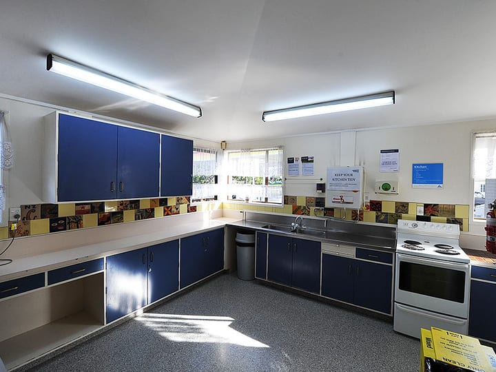 Community kitchen with blue cabinetry, stainless sink, and decorative tiled splashback