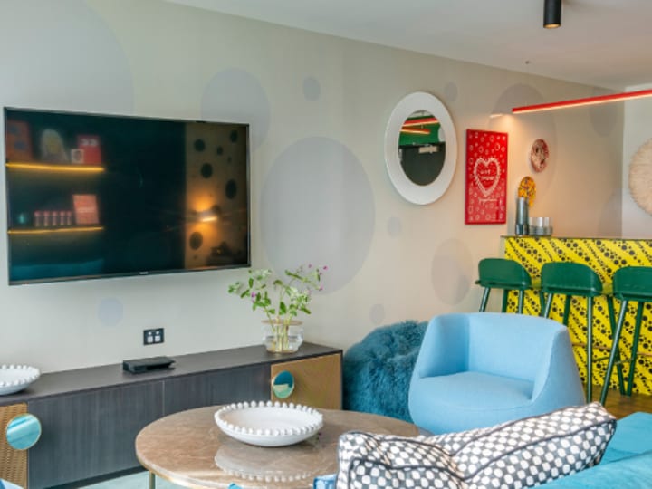 Colourful lounge area with blue sofa, yellow bar, green bar stools, and eclectic wall art