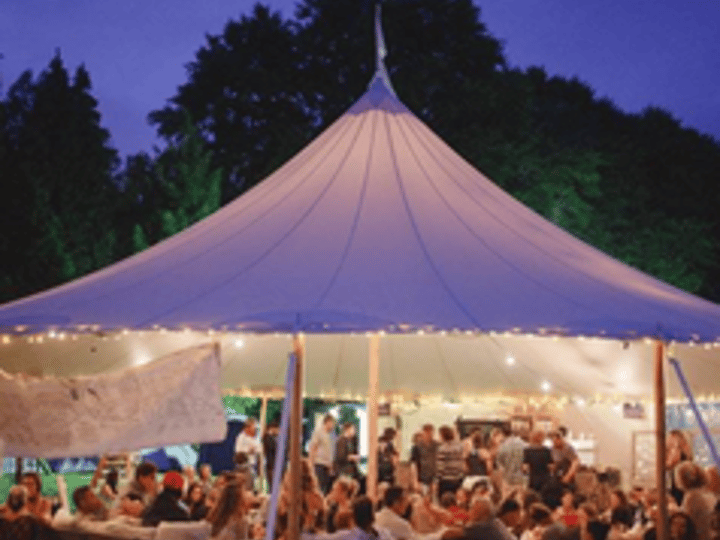 Marquee lit at night with guests seated inside under tall pole tent