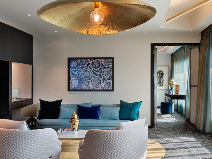 Dramatic hotel suite lounge with large gold pendant, teal sofa, patterned artwork, and rich textiles