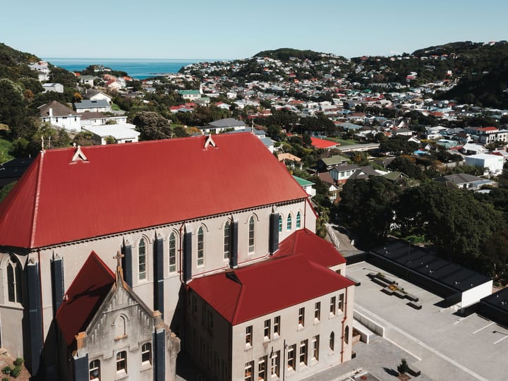 Wide aerial view of Gothic stone chapel with red roof and surrounding suburb