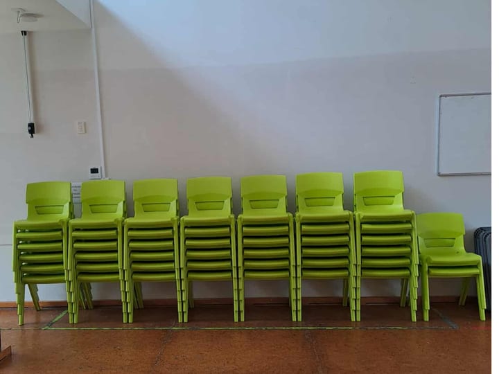 Stacked green plastic chairs against a white wall with whiteboard