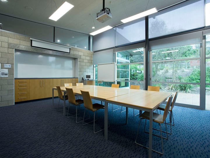 Meeting room with long table, chairs, projector screen, and garden view