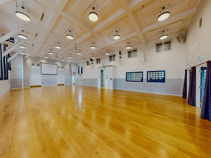 Large empty hall with polished timber floor, coffered ceiling, and pendant lights