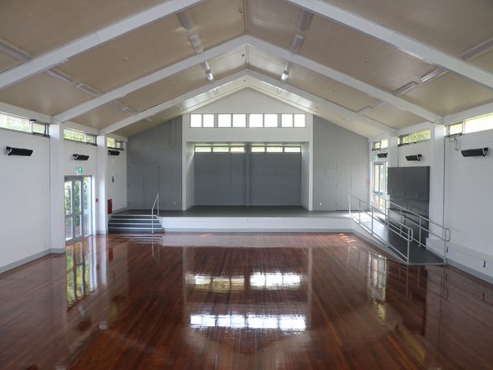Hall interior with vaulted ceiling, polished timber floor, and raised platform at far end with ramp